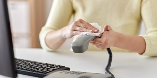 hygiene and disinfection concept - close up of woman hands cleaning desk phone with paper tissue